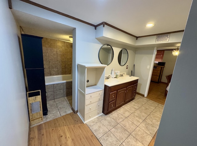 bathroom with hardwood / wood-style floors, vanity, tiled bath, and ornamental molding