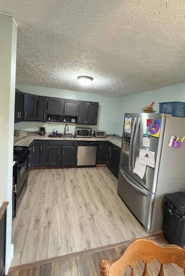 kitchen featuring a textured ceiling, sink, stainless steel appliances, and light hardwood / wood-style flooring