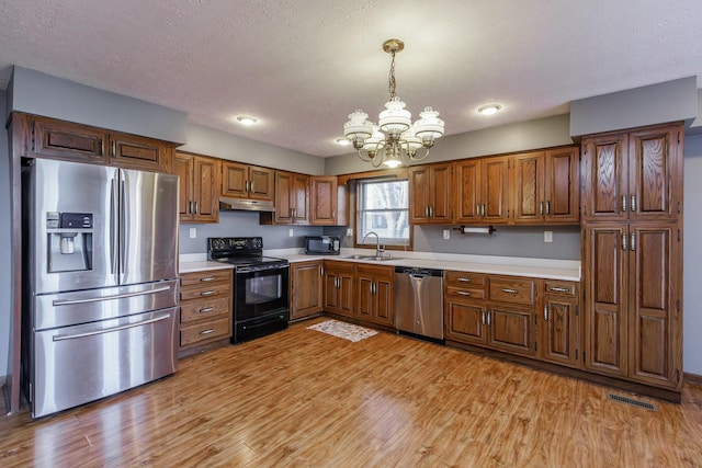 kitchen with a chandelier, pendant lighting, black appliances, and light hardwood / wood-style flooring