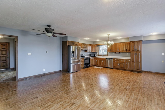 kitchen featuring ceiling fan with notable chandelier, a textured ceiling, stainless steel appliances, pendant lighting, and light hardwood / wood-style flooring