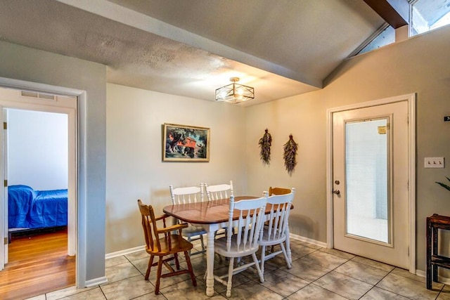 dining room featuring a textured ceiling, light tile patterned floors, and lofted ceiling