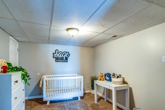 bedroom with dark carpet, a crib, and a drop ceiling