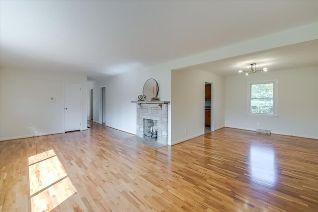 unfurnished living room featuring a fireplace, light wood-type flooring, and a notable chandelier