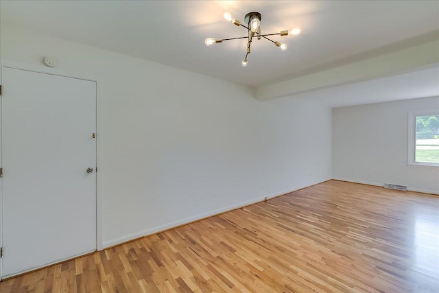 empty room featuring beamed ceiling, a notable chandelier, and light hardwood / wood-style floors