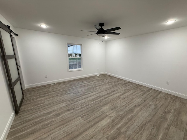 spare room featuring a barn door, hardwood / wood-style flooring, and ceiling fan