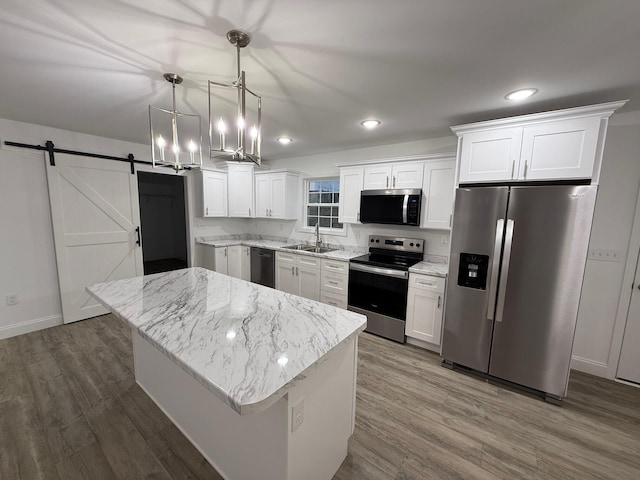 kitchen with appliances with stainless steel finishes, a barn door, white cabinets, a kitchen island, and hanging light fixtures