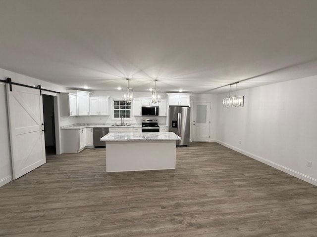 kitchen with sink, hanging light fixtures, stainless steel appliances, a barn door, and a kitchen island