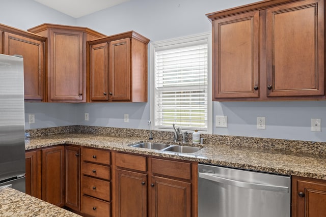 kitchen featuring brown cabinets, stone countertops, stainless steel appliances, and a sink