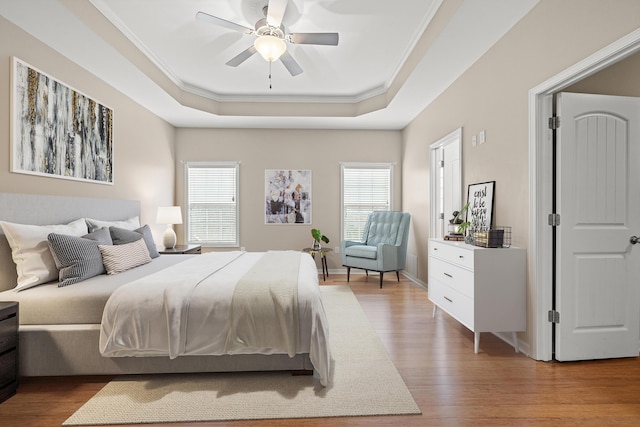 bedroom featuring a raised ceiling, crown molding, multiple windows, and wood finished floors