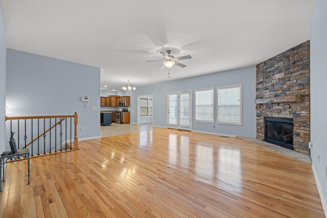 living room with ceiling fan with notable chandelier, a fireplace, and light hardwood / wood-style floors