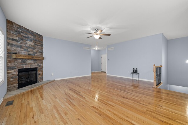 unfurnished living room with a stone fireplace, ceiling fan with notable chandelier, and light hardwood / wood-style flooring