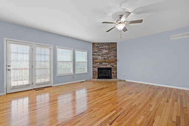 unfurnished living room featuring ceiling fan, a stone fireplace, and light hardwood / wood-style floors