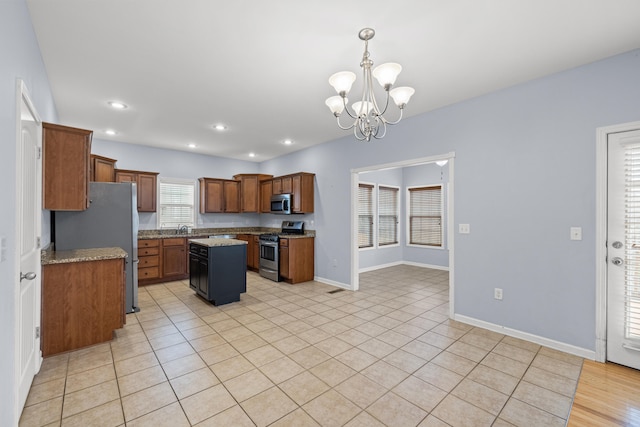 kitchen featuring appliances with stainless steel finishes, decorative light fixtures, a center island, a notable chandelier, and light stone countertops