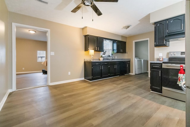 kitchen featuring stainless steel electric range, sink, ceiling fan, independent washer and dryer, and light wood-type flooring