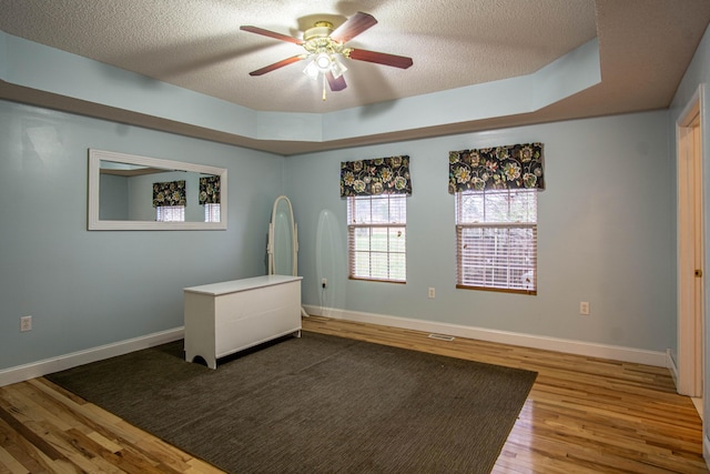 spare room with a tray ceiling, ceiling fan, wood-type flooring, and a textured ceiling