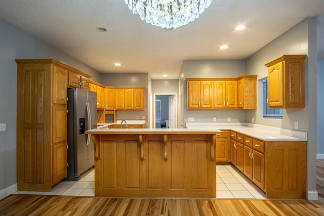 kitchen featuring light wood-type flooring, sink, a notable chandelier, stainless steel fridge with ice dispenser, and an island with sink