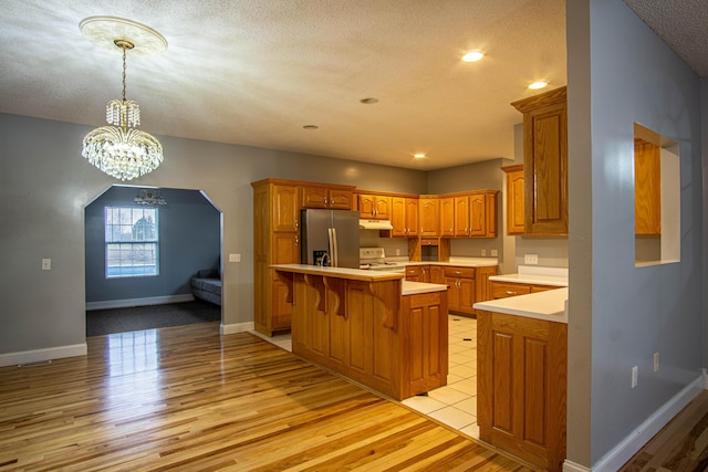 kitchen featuring a center island, light wood-type flooring, white range oven, stainless steel fridge with ice dispenser, and a breakfast bar area