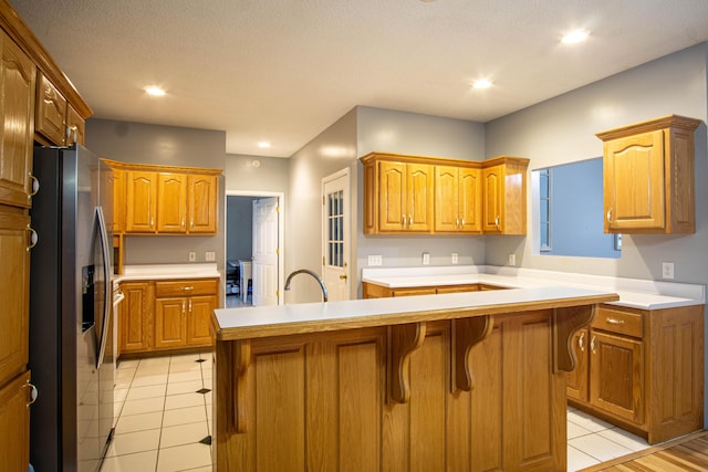 kitchen featuring stainless steel refrigerator with ice dispenser, a center island with sink, a kitchen breakfast bar, and light tile patterned flooring