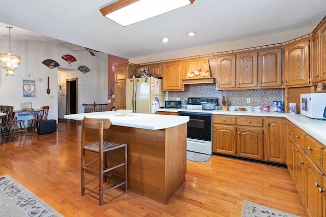 kitchen with decorative backsplash, hanging light fixtures, light hardwood / wood-style floors, and white appliances