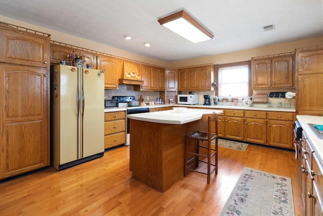 kitchen with decorative backsplash, a center island, white appliances, and light hardwood / wood-style flooring