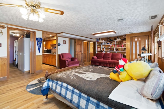 bedroom featuring ceiling fan, light hardwood / wood-style flooring, crown molding, wood walls, and a textured ceiling