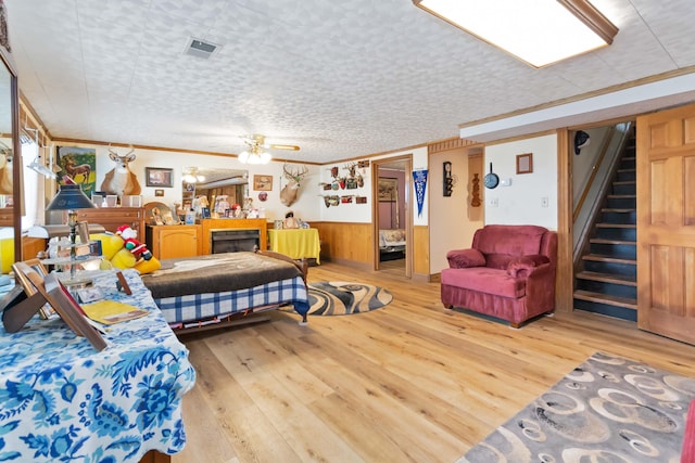 bedroom with ceiling fan, light hardwood / wood-style floors, a textured ceiling, wooden walls, and ornamental molding