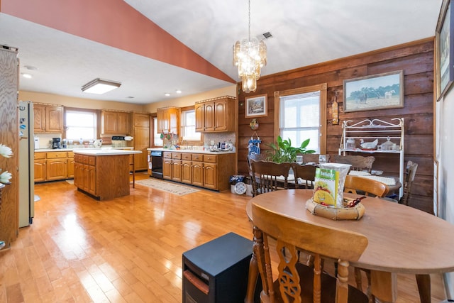 dining area featuring light wood-type flooring, an inviting chandelier, vaulted ceiling, and wood walls