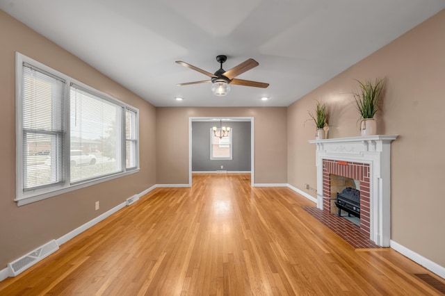 unfurnished living room featuring light hardwood / wood-style floors, ceiling fan with notable chandelier, and a brick fireplace