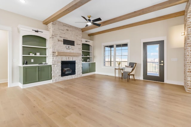 unfurnished living room featuring ceiling fan, beam ceiling, a fireplace, light hardwood / wood-style floors, and built in shelves