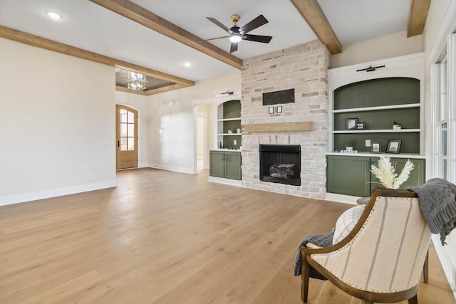 living room featuring a stone fireplace, built in features, beamed ceiling, hardwood / wood-style flooring, and ceiling fan