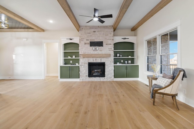 living room with built in features, ceiling fan, beam ceiling, a fireplace, and light wood-type flooring