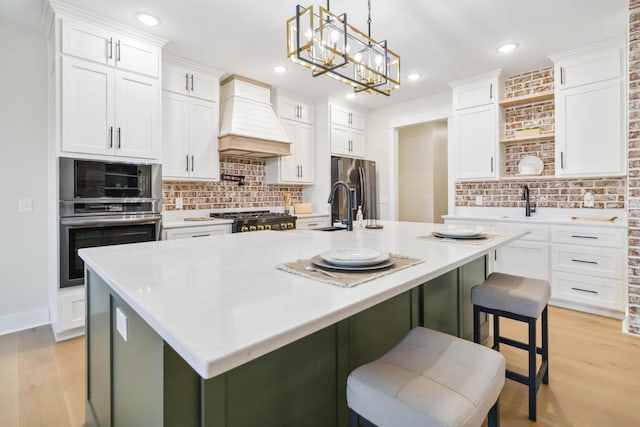 kitchen with a kitchen island with sink, white cabinets, and premium range hood