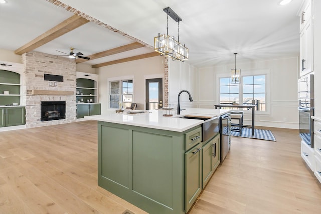 kitchen with sink, white cabinetry, green cabinetry, decorative light fixtures, and a center island with sink