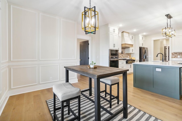 kitchen with decorative light fixtures, white cabinets, stainless steel appliances, custom range hood, and an inviting chandelier