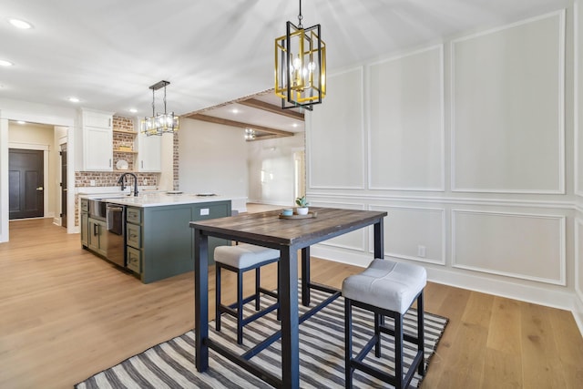 kitchen featuring pendant lighting, white cabinetry, backsplash, a center island with sink, and light hardwood / wood-style flooring