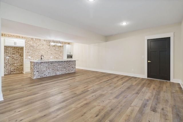 unfurnished living room featuring brick wall, sink, and light hardwood / wood-style floors