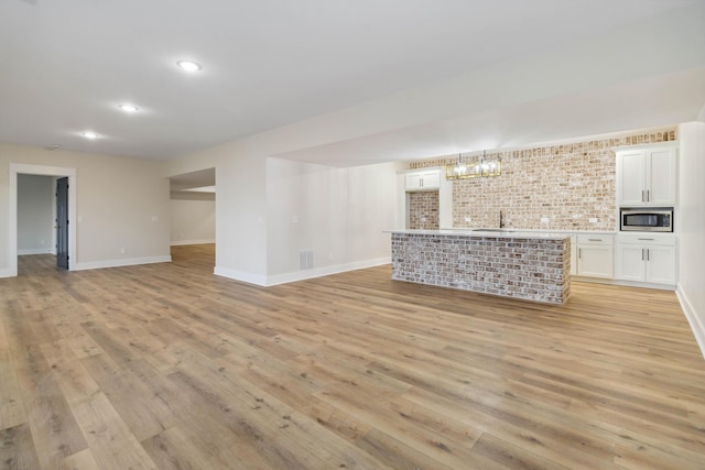 unfurnished living room featuring brick wall, sink, and light wood-type flooring