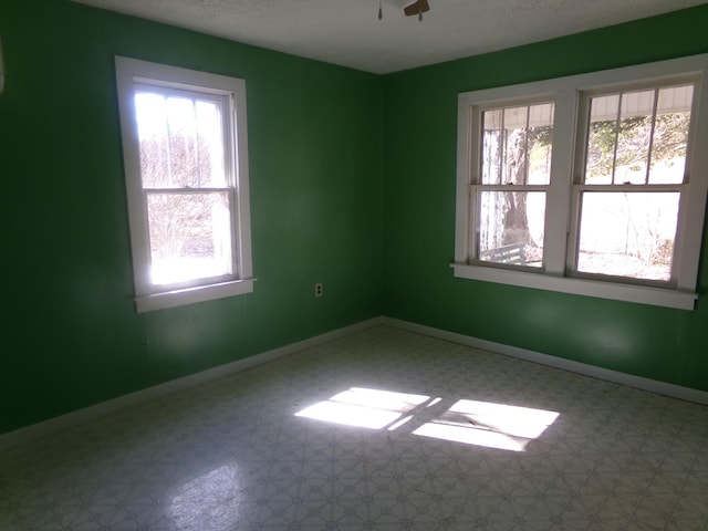 unfurnished room with a healthy amount of sunlight, ceiling fan, baseboards, and tile patterned floors