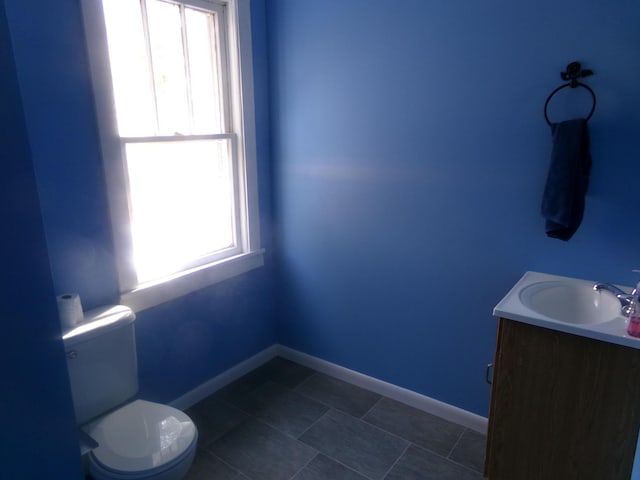 half bathroom with toilet, plenty of natural light, baseboards, and vanity