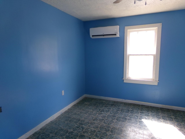 unfurnished room featuring a wall unit AC, ceiling fan, baseboards, and a textured ceiling