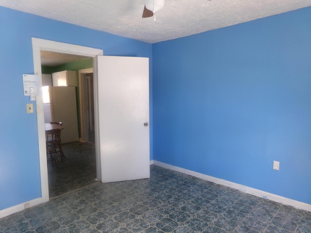 empty room with ceiling fan, a textured ceiling, and baseboards