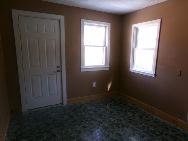 unfurnished room with baseboards, a textured ceiling, and a healthy amount of sunlight