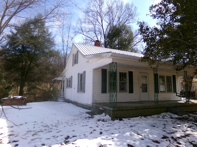 view of front of house featuring a porch, a standing seam roof, metal roof, and a chimney