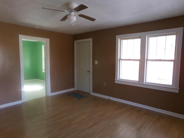 spare room with a textured ceiling, a ceiling fan, light wood-style flooring, and baseboards