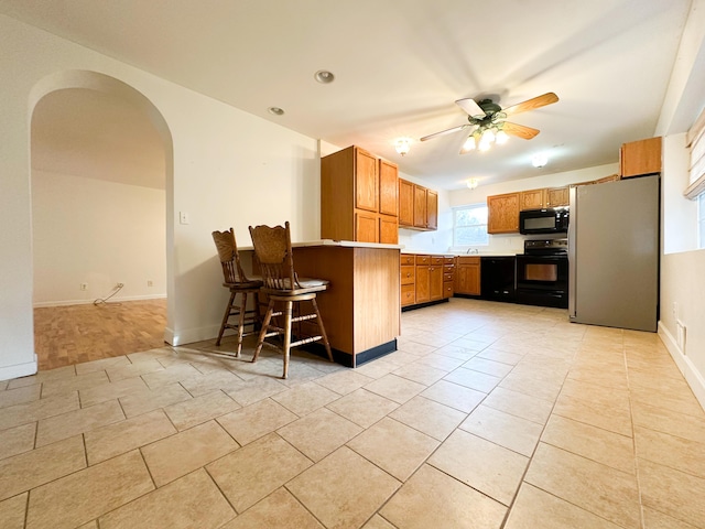 kitchen with a breakfast bar area, light tile patterned floors, kitchen peninsula, ceiling fan, and black appliances