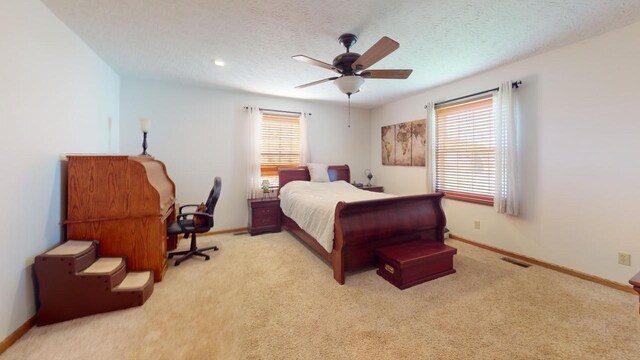 bedroom with ceiling fan, a textured ceiling, light carpet, and multiple windows