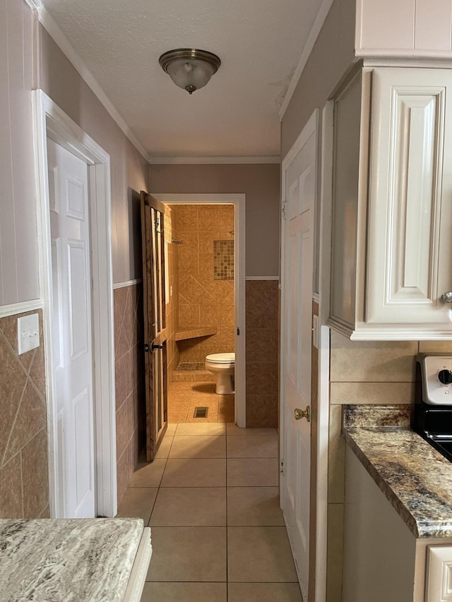 hall with light tile patterned floors, visible vents, ornamental molding, tile walls, and a wainscoted wall