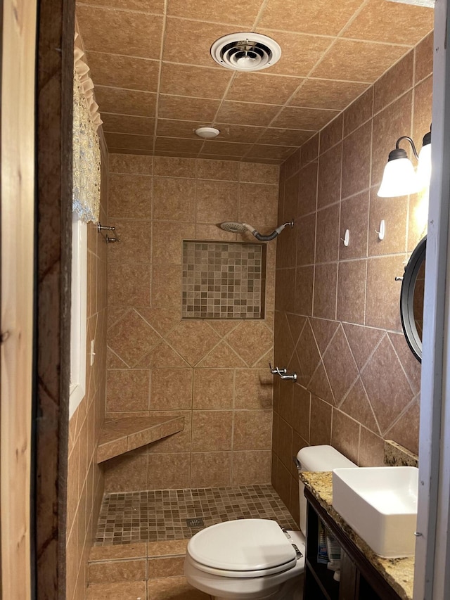 bathroom featuring vanity, toilet, tile walls, and a tile shower