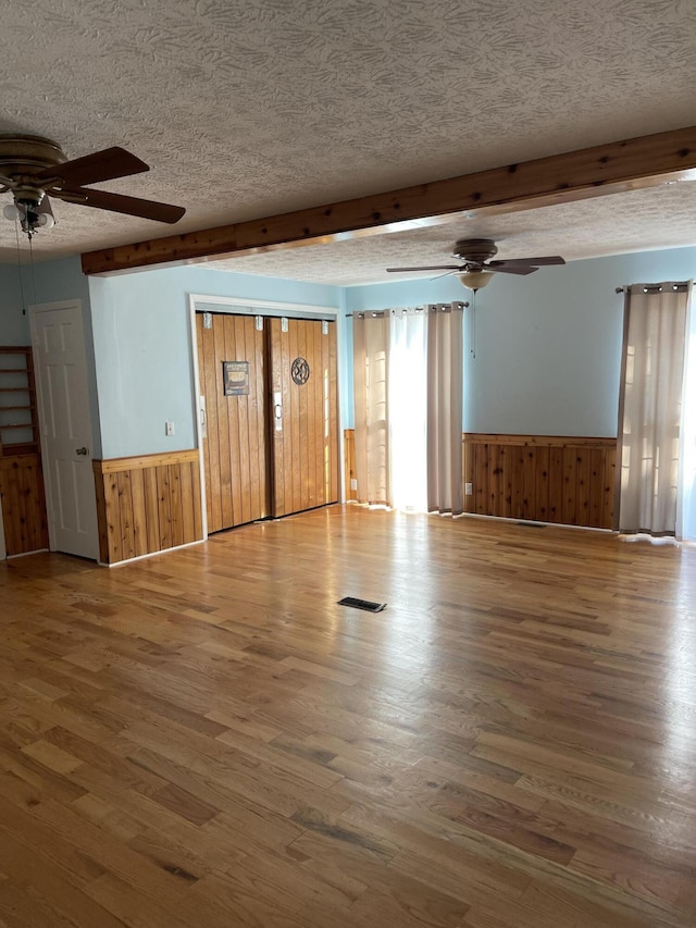 unfurnished room featuring a textured ceiling, ceiling fan, wooden walls, hardwood / wood-style flooring, and beamed ceiling