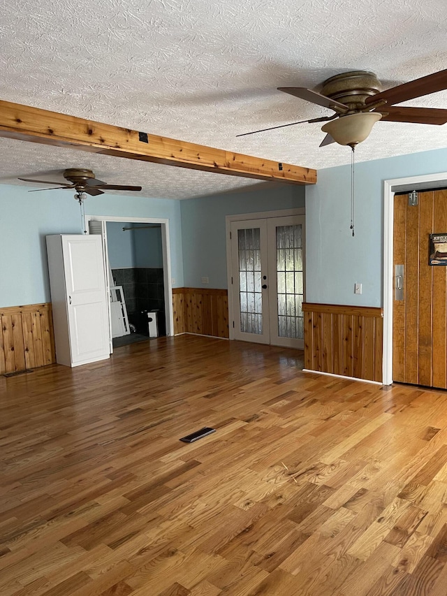 unfurnished living room with wooden walls, a wainscoted wall, a ceiling fan, and a textured ceiling